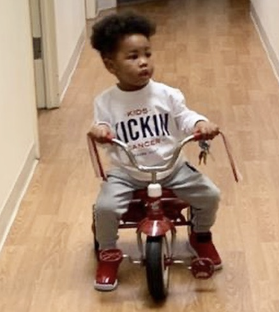 Cancer Kickers Teammate Kolton riding a trike wearing player kit long sleeve white shirt with logo nike label looking up