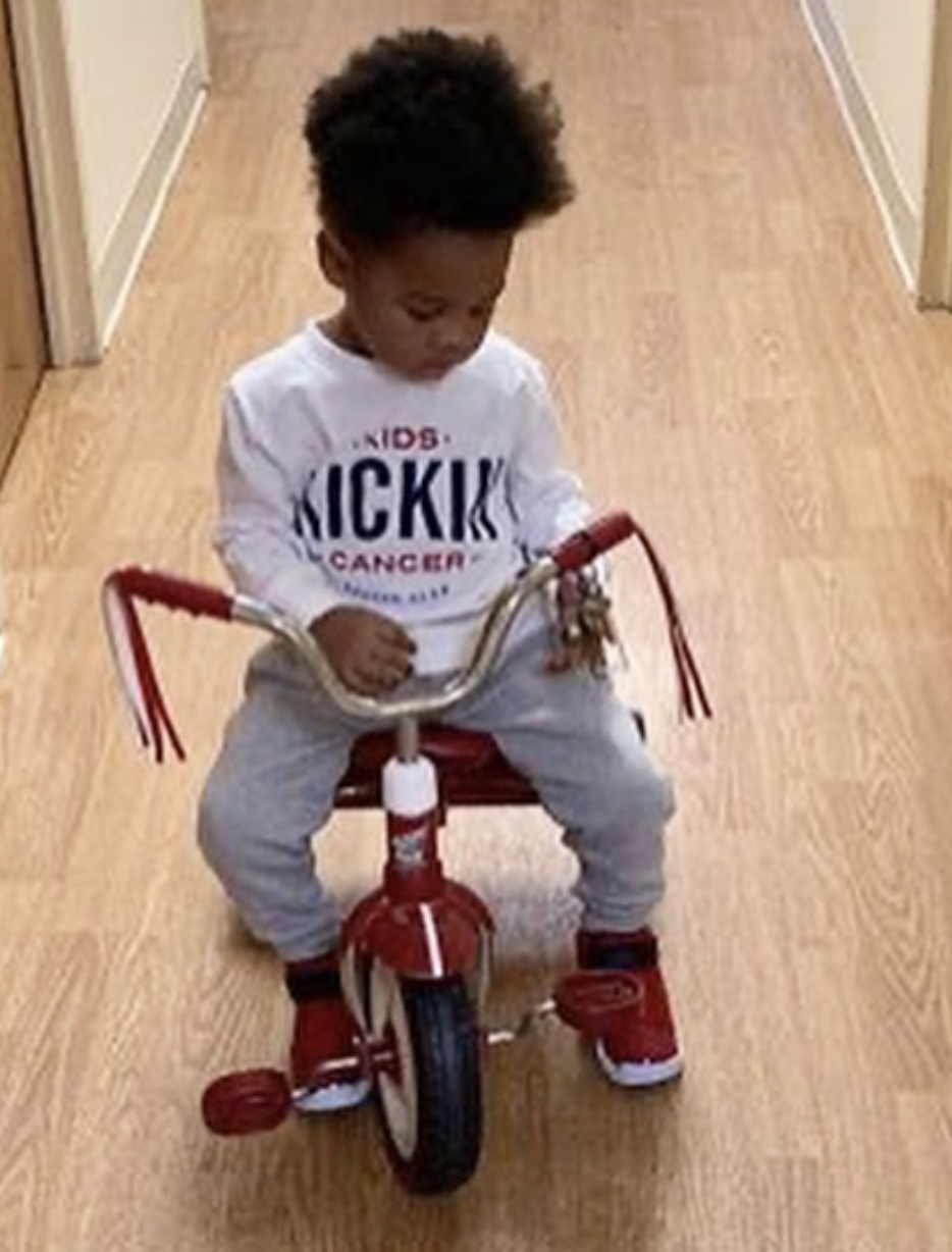 Cancer Kickers Teammate Kolton riding a trike wearing player kit long sleeve white shirt with logo nike label looking down