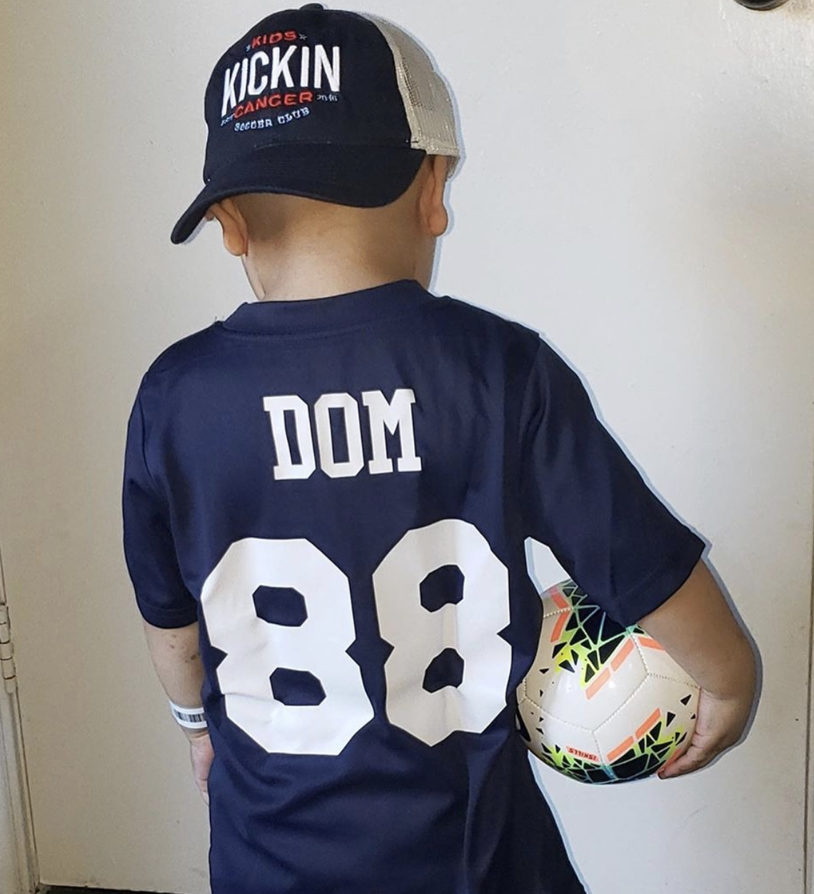 cancer kickers Teammate Domonic wearing custom name and number jersey holding nike ball