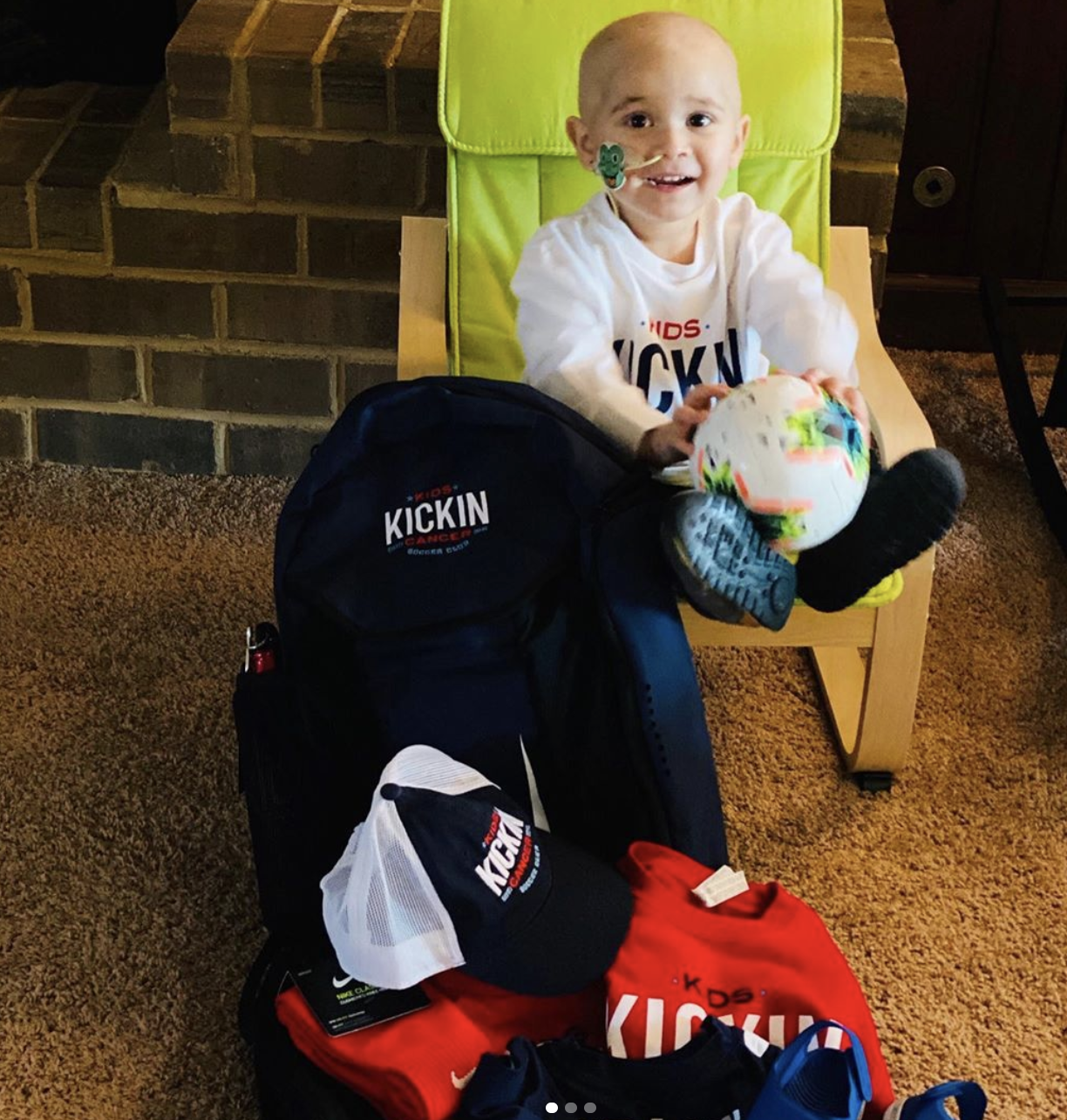 Cancer Kickers Teammate Griffin smiling sitting in chair surrounded by player kit gear with soccer ball hat t-shirt nike label